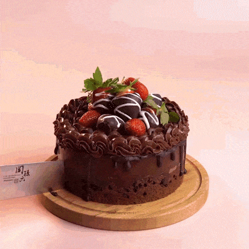 A chocolate cake topped with strawberries is cut into slices.
