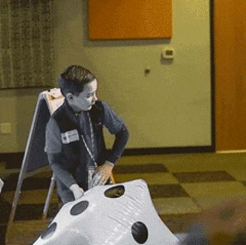 A boy throws a giant inflatable die across a room.