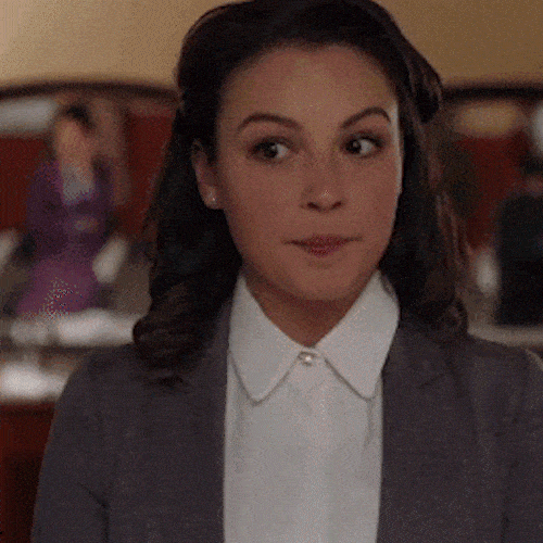 A woman in a white collared shirt and dark jacket glances sideways with a doubtful look.