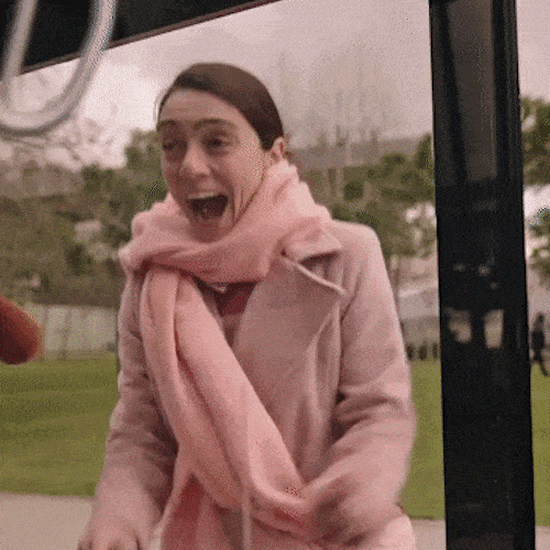 Woman in a pink coat reacting with open-mouthed excitement