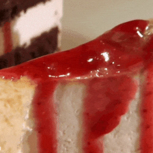 A close-up of a slice of layered cake topped with strawberries and red syrup.