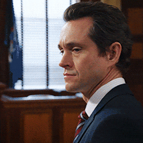 A man in a suit in a courtroom turns and nods firmly.