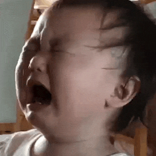A baby cries loudly with eyes squeezed shut.