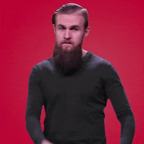 A bearded man in a black shirt points and then mimes a phone call with his hand.