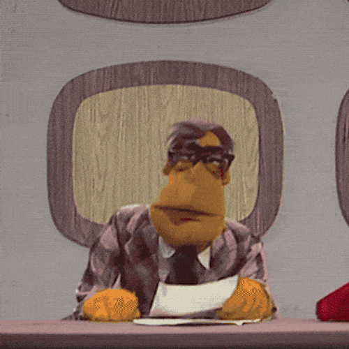 A puppet news anchor at a desk is interrupted by a puppet bird flying past.