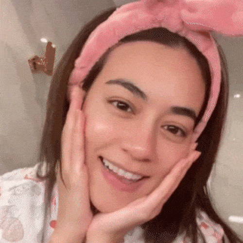 Woman with a pink headband holding her face and smiling