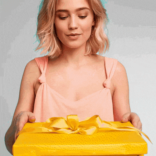 A young woman opens a yellow gift box full of euro banknotes and holds them up in delight.