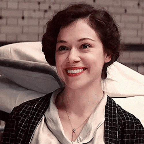 A smiling woman with dark curly hair laughs and tilts her head.