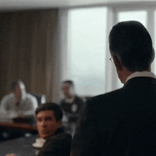 A man in a meeting room raises his fist in triumph as his colleagues cheer.