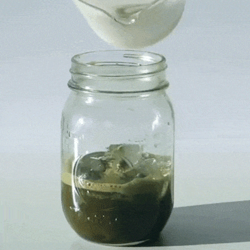 Milk is poured into a glass jar of iced coffee.