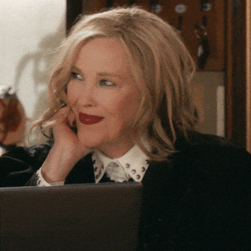 A blonde woman rests her chin on her hand and presses a finger to her lips.