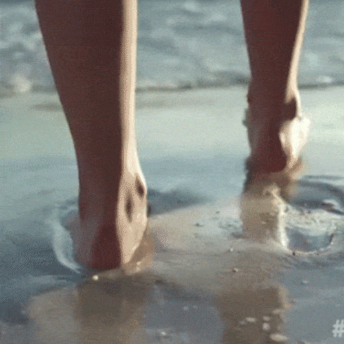 Bare feet walk through shallow water on a beach.