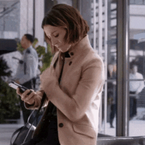 Woman in a coat looking at her phone in a modern office setting