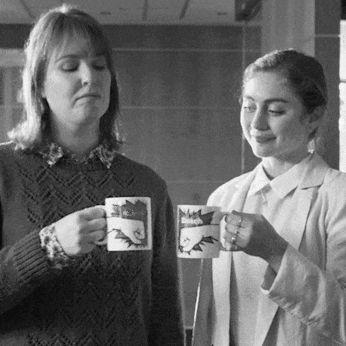 Two women chat over cups of tea in a black-and-white scene.