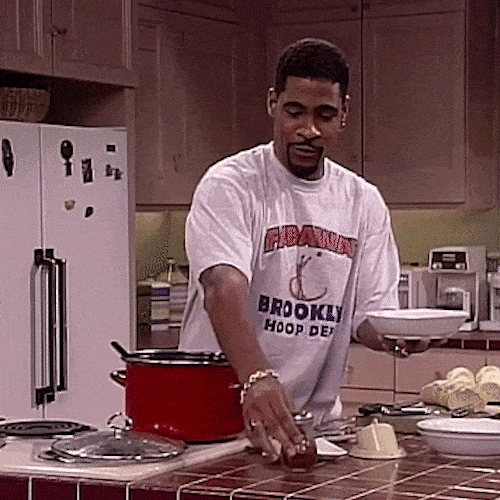 A man in a kitchen presents a plate with a dramatic flourish of his hand.
