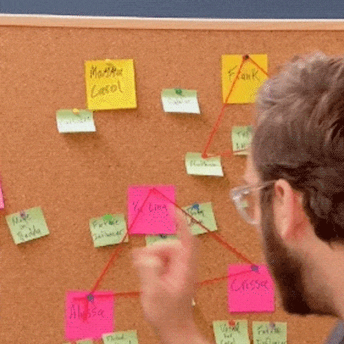 A man pins colorful sticky notes connected with red string to a corkboard.