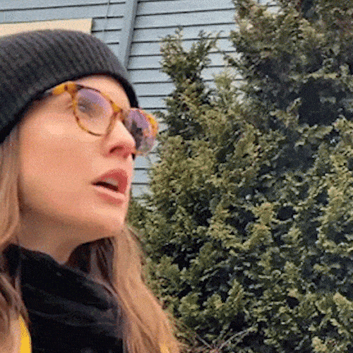 A woman in a beanie and glasses breathes out, and her breath shows as mist in the cold air.