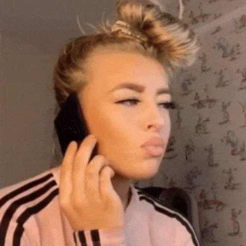 A woman holds a phone to her ear, spelling something out loud.