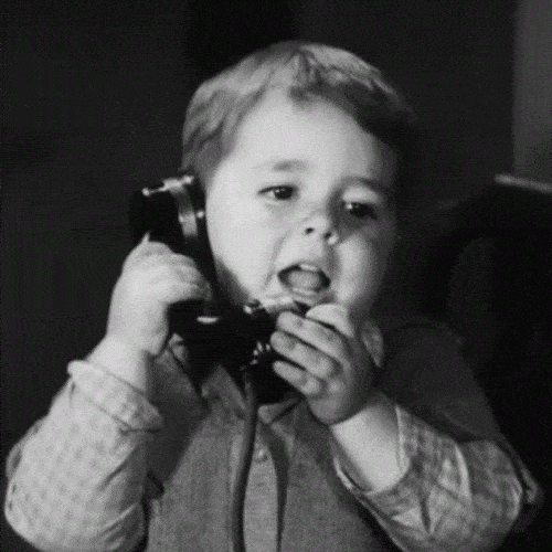 A black-and-white photo of a young boy speaking into an old telephone receiver.
