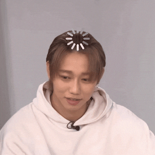 A young man in a white hoodie looks down while a loading icon spins on top of his head.