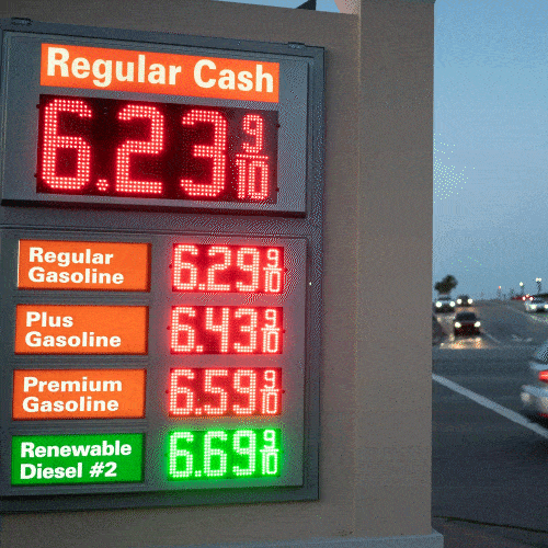 An illuminated gas station price sign displays prices for regular, plus, premium, and diesel fuel.