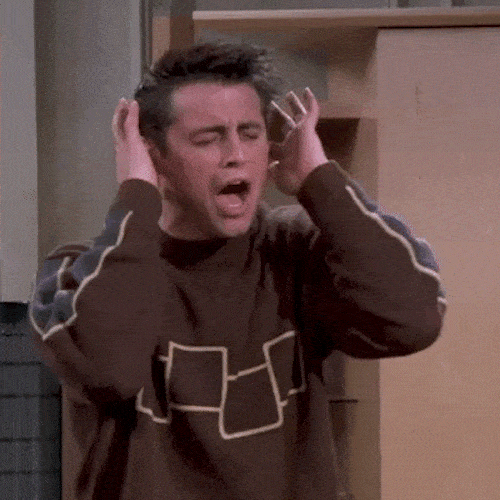A man in a brown sweater holds his head in his hands and shouts in frustration.