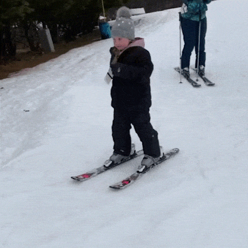 A small child in a winter hat skis down a snowy slope.