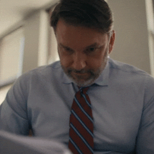 &bull;	Man in office attire looking down while carefully reviewing a document
