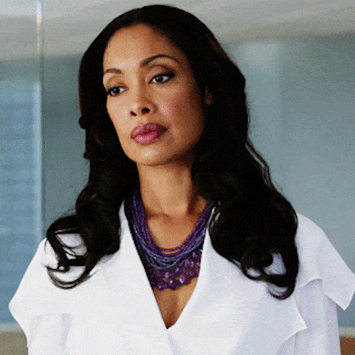 A confident woman with long dark hair in a white blazer looks straight ahead.