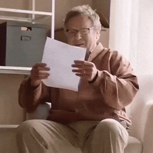 A man in an armchair tears a sheet of paper into pieces.