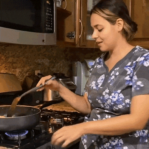 A woman stirs food in a pan on the stove.