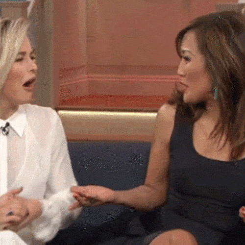 Two women sit on a couch, hugging each other.