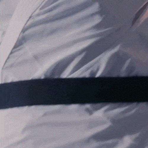 A close-up of a black belt being tied tightly around a white martial arts uniform.