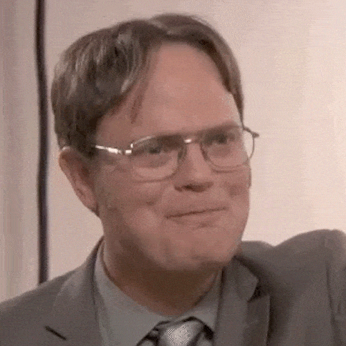 A man in glasses and a suit gives a small, satisfied smile.