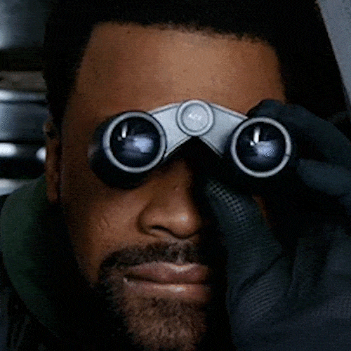 A man looks through a pair of binoculars and frowns.