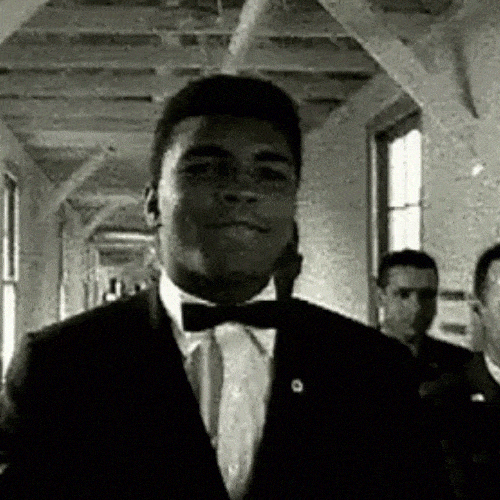 Black-and-white GIF of a man walking confidently in a suit.