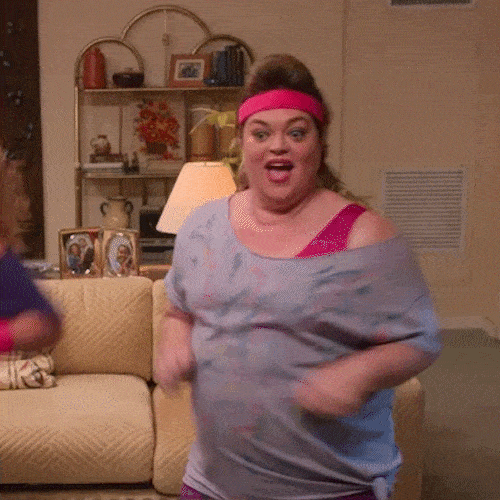 A woman in a pink headband dances energetically in her living room as a workout.