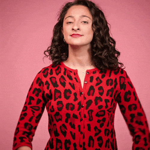 A woman in a red leopard-print top smiles, puts a hand on her chest, and takes a small bow.