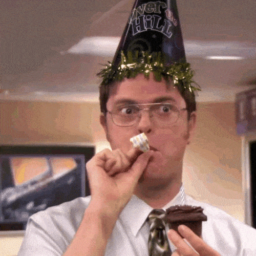 Man in a party hat blowing a noisemaker and holding cake