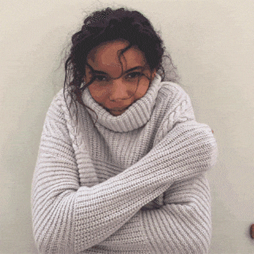 A woman bundled in a chunky knit sweater hugs herself to keep warm.