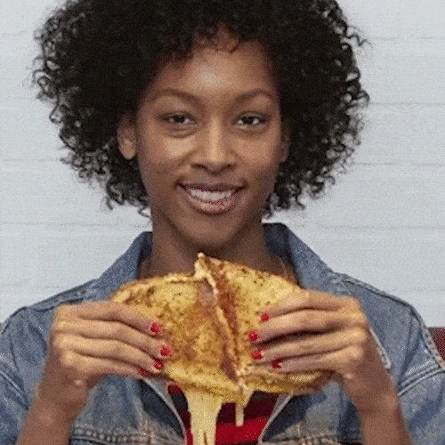 A smiling woman pulls apart a grilled cheese sandwich, stretching the melted cheese.