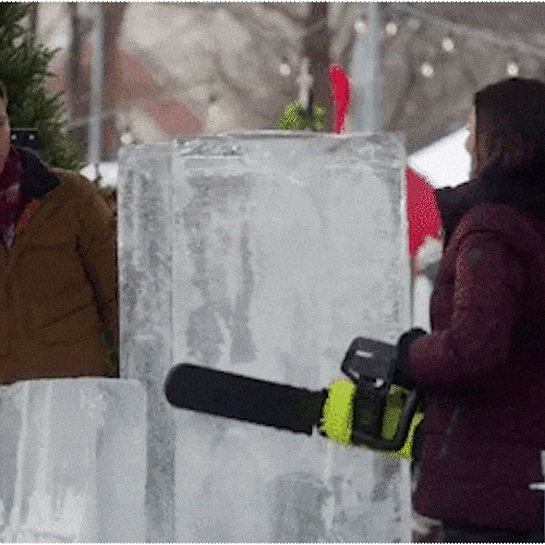 A person cuts into a large block of ice with a chainsaw.