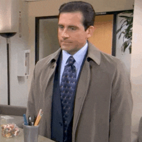 Man in a coat and tie standing in an office with a sheepish look