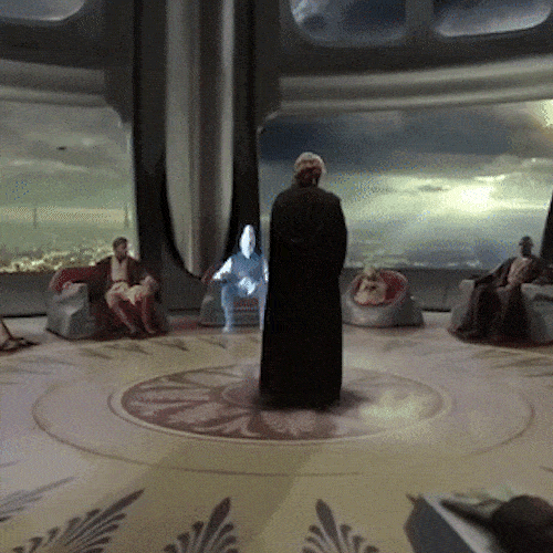 A hooded figure stands in the middle of a circular chamber, surrounded by a seated council.
