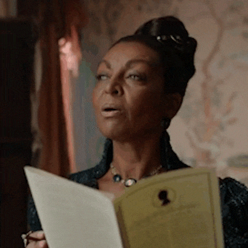 A woman in a dark dress reads a card and smirks with satisfaction.