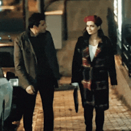 A man and a woman in coats walk side by side down a street at night.