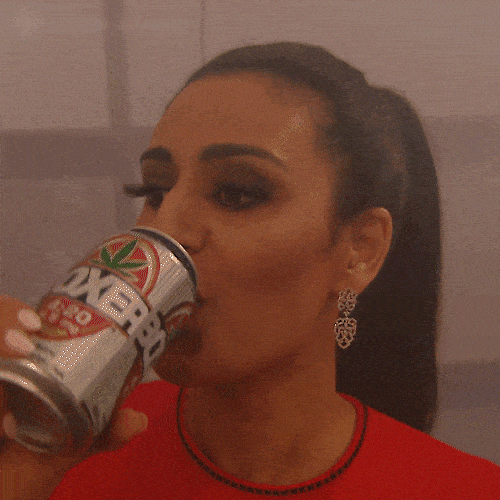 A woman with a ponytail drinks from a can with green and red branding. 